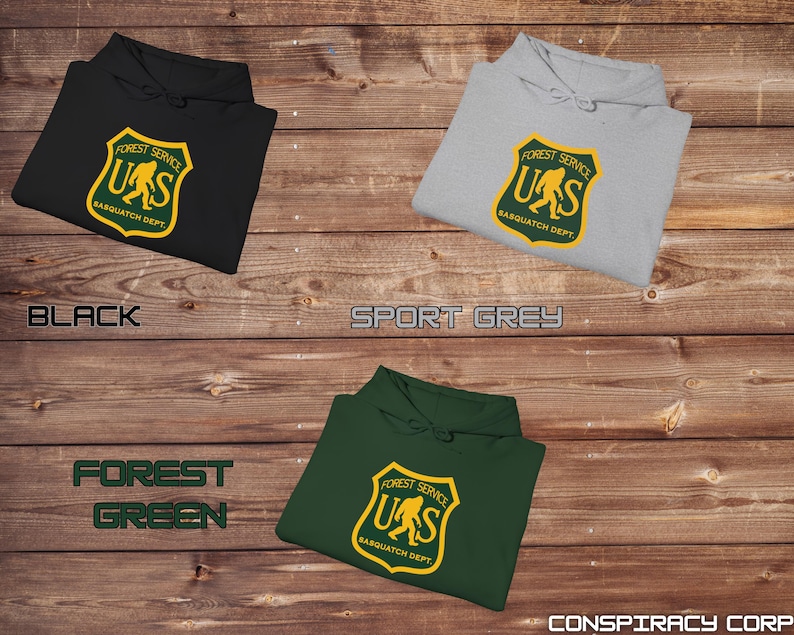 May include: Three hooded sweatshirts in black, forest green, and sport grey with a graphic print of a yellow Sasquatch inside a yellow shield with the text "Forest Service US Sasquatch Dept."
