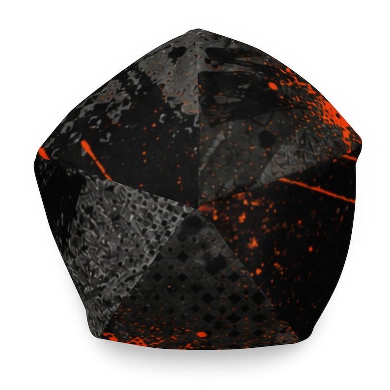 Top view of black and orange graphic beanie showing paneled construction, distressed urban artwork, charcoal textures and bright orange graffiti details.
