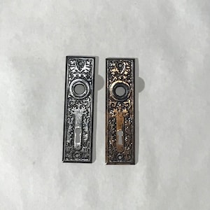 May include: Two ornate door knobs with a keyhole in the center. One is black and the other is gold.