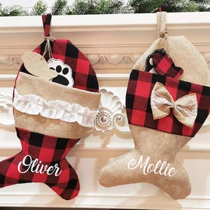 May include: Two fish-shaped Christmas stockings. One is red and black buffalo plaid with the name "Oliver" in white script. The other is tan burlap with a red and black plaid cuff and a bow, with the name "Mollie".
