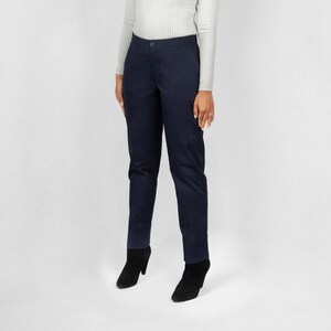 May include: A woman wearing a white ribbed turtleneck sweater and dark blue pants. She is standing on a white background.