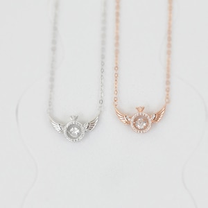 May include: Two delicate necklaces with a sparkling crystal pendant in the center. The pendant is surrounded by smaller crystals and has a small crown on top. The necklaces are on a white background. One necklace is silver and the other is rose gold.