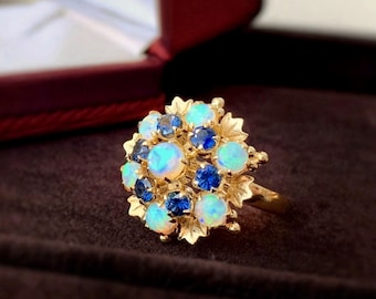 May include: A gold ring with a cluster of opal and sapphire gemstones. The ring is set in a floral design.