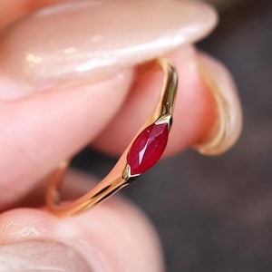 Peut inclure: Une bague en or ornée d'un rubis de forme marquise. Le rubis est d'un rouge profond et est serti dans un fin anneau en or. La bague est de conception simple et élégante.