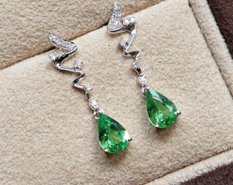 May include: A pair of elegant drop earrings. Each earring features a silver-toned, wavy design adorned with small, sparkling stones. The earrings culminate in a vibrant, pear-shaped, emerald-green gemstone, creating a sophisticated and eye-catching accessory.