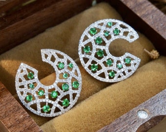 May include: A pair of silver earrings with a geometric design featuring green gemstones. The earrings are in a small wooden box.