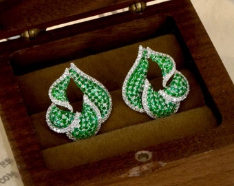 May include: A pair of green and white diamond earrings in the shape of a leaf, displayed in a wooden box.