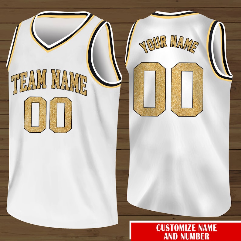 Puede incluir: Camiseta de baloncesto blanca con ribetes negros y dorados. La parte delantera de la camiseta tiene el texto "TEAM NAME" y el n&uacute;mero "00" en purpurina dorada. La parte trasera de la camiseta tiene el texto "YOUR NAME" y el n&uacute;mero "00" en purpurina dorada.
