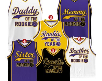 Puede incluir: Conjunto de seis camisetas de baloncesto en varios colores con el texto "Daddy of the Rookie", "Mommy of the Rookie", "Rookie of the Year", "Sister of the Rookie", "Cousin of the Rookie" y "Brother of the Rookie".