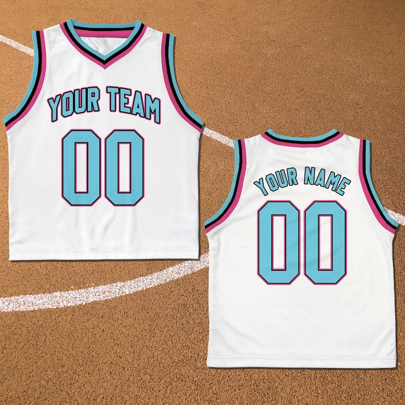 May include: White basketball jersey with black and pink trim. The front of the jersey has the text "YOUR TEAM" and the number "00" in light blue. The back of the jersey has the text "YOUR NAME" and the number "00" in light blue.