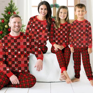 Pode incluir: Conjuntos de pijama de manga comprida a combinar com um padrão xadrez vermelho, verde e preto, com pequenos gráficos natalícios incluindo bonecos de neve, renas e caras do Pai Natal. Os conjuntos incluem camisolas de gola redonda e calças.