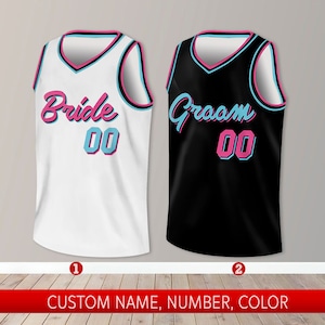 May include: Two basketball jerseys, one white with "Bride 00" in pink and blue lettering, and one black with "Groom 00" in pink and blue lettering.