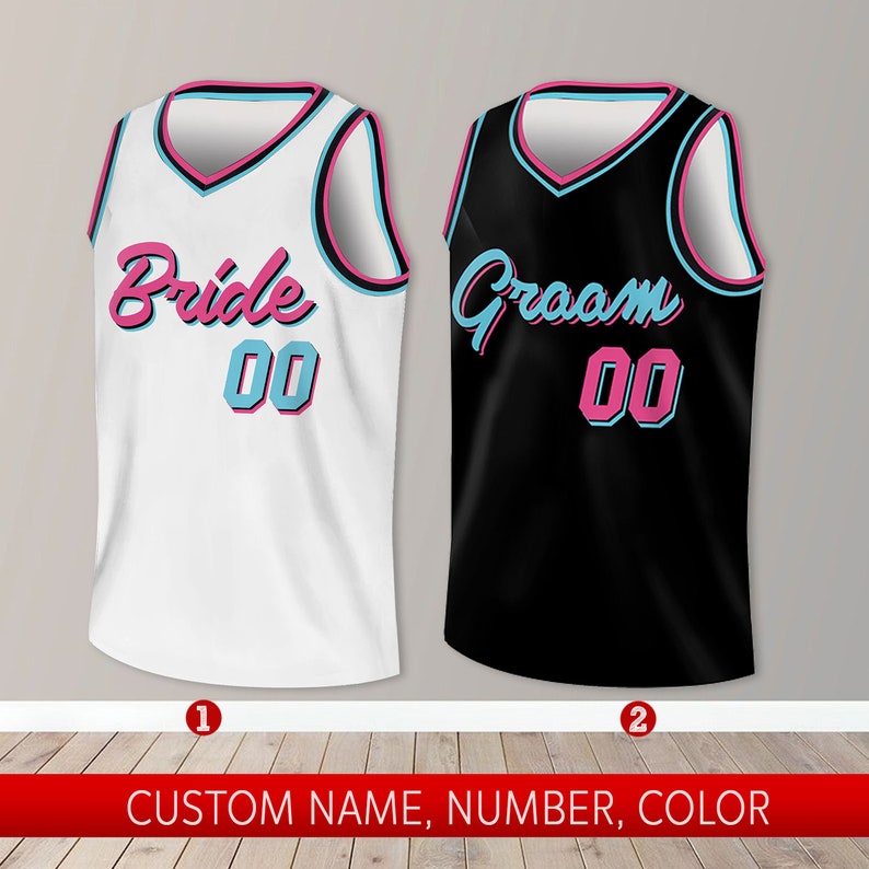 May include: Two basketball jerseys, one white with "Bride 00" in pink and blue lettering, and one black with "Groom 00" in pink and blue lettering.