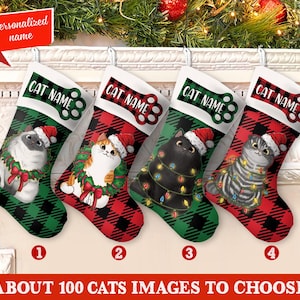 以下が含まれることがあります： 猫のデザインが施された4つのクリスマスストッキング。各ストッキングには、サンタの帽子とお祝いのリースを身に着けたさまざまな猫が描かれています。ストッキングは赤と緑のチェック柄です。ストッキングのテキストは「CAT NAME」です。