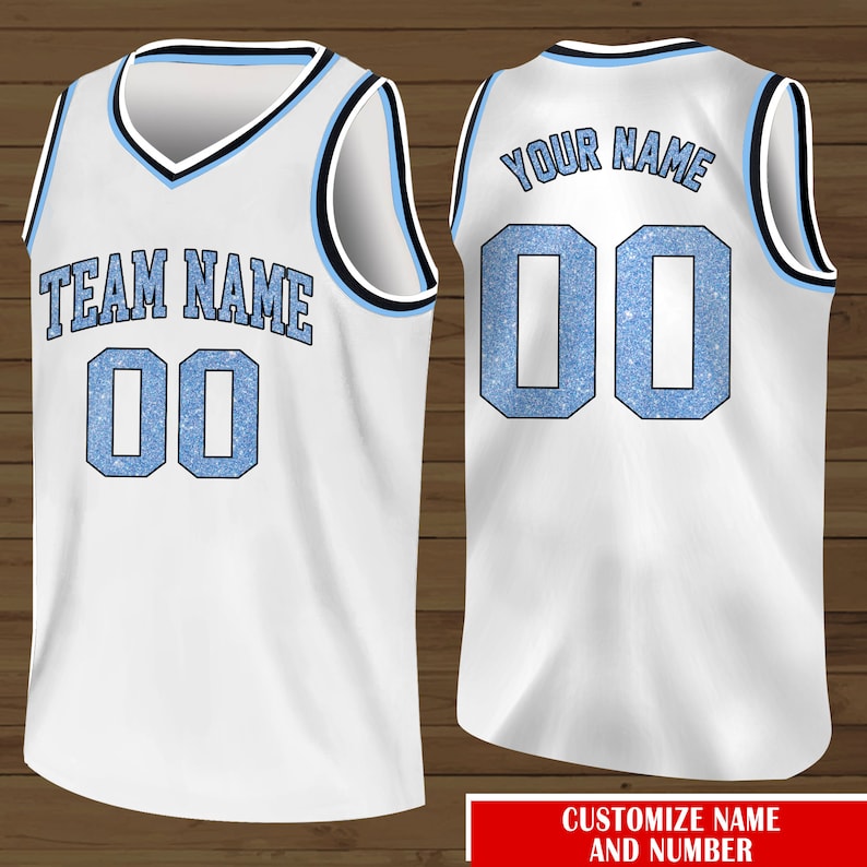 Puede incluir: Camiseta de baloncesto blanca con ribetes azules y negros. La parte delantera de la camiseta tiene el texto "TEAM NAME" y el n&uacute;mero "00" en azul con un efecto brillante. La parte trasera de la camiseta tiene el texto "YOUR NAME" y el n&uacute;mero "00" en azul con un efecto brillante.
