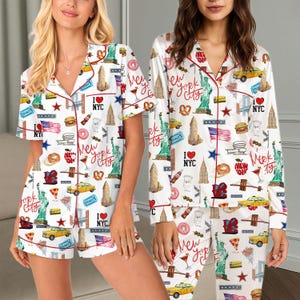 May include: White pyjama sets with a New York City theme. The sets feature a repeating pattern of iconic landmarks, food, and symbols of NYC. The short-sleeved set has shorts, and the long-sleeved set has trousers. Both sets have red trim.