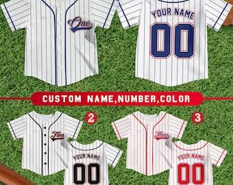 Puede incluir: Tres camisetas de béisbol blancas con rayas azules, rojas y negras. Las camisetas tienen los números "00" y las palabras "One", "Two" y "Three" en ellas. Las camisetas están sobre un fondo de hierba verde.
