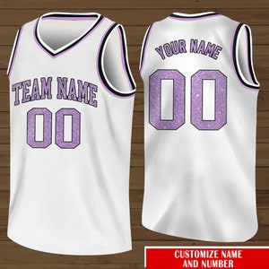 Puede incluir: Camiseta de baloncesto blanca con ribetes negros y morados. La parte delantera de la camiseta tiene el texto "TEAM NAME" y el n&uacute;mero "00" en purpurina morada. La parte trasera de la camiseta tiene el texto "YOUR NAME" y el n&uacute;mero "00" en purpurina morada.