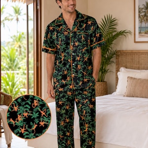 May include: A black pajama set featuring a short-sleeved button-down shirt and long pants with an all-over print of orange monkeys and green palm leaves. The shirt includes a notched collar and orange piping along the edges and front closure.