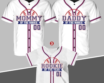 Könnte beinhalten: Drei weiße Baseballtrikots mit roten und blauen Verzierungen. Das erste Trikot trägt die Aufschrift "Mommy of the Rookie 00". Das zweite Trikot trägt die Aufschrift "Daddy of the Rookie 00". Das dritte Trikot trägt die Aufschrift "Rookie of the Year 01".