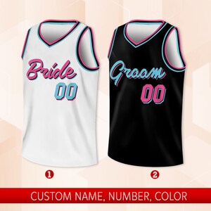 May include: Two basketball jerseys, one white with "Bride 00" in pink and blue lettering, and one black with "Groom 00" in pink and blue lettering.