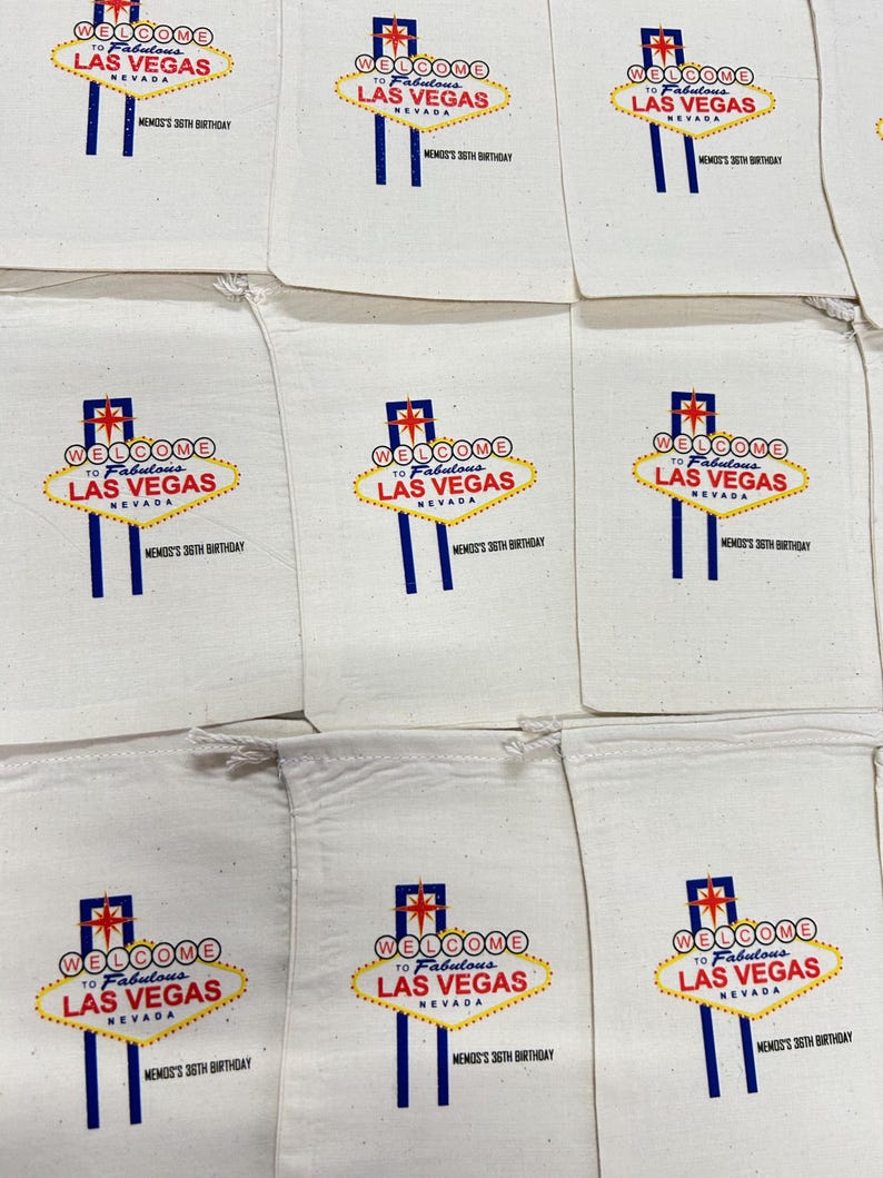 K&ouml;nnte beinhalten: Eine Ansammlung von beigefarbenen Baumwollbeuteln mit Kordelzug, die jeweils mit dem Welcome to Fabulous Las Vegas-Schild in Rot, Blau und Gelb bedruckt sind, wobei der Text MEMO'S 36TH BIRTHDAY in Schwarz unter dem Motiv steht.