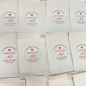 K&ouml;nnte beinhalten: Eine Sammlung von cremefarbenen Baumwollbeuteln mit Kordelzug, bedruckt mit einem roten Herz, einem Kreuz und dem Text "IN SICKNESS & IN HEALTH HANGOVER Kit", gefolgt von den Namen "&Aacute;LVARO & ELENA" und dem Datum "18/10/2025".