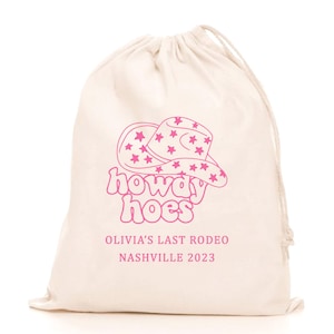 May include: A white cotton drawstring bag with a pink graphic of a cowboy hat with stars and the text "howdy hoes" printed on it. The bag also has the text "Olivia's Last Rodeo Nashville 2023" printed on it.