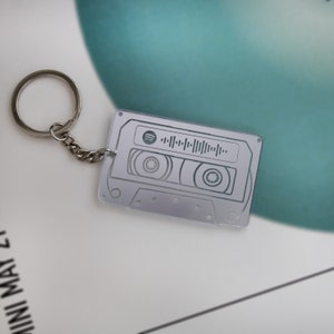 May include: A silver keychain shaped like a cassette tape with a Spotify logo and a barcode on the front.