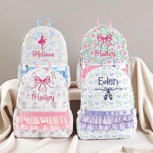 May include: Four backpacks featuring floral and butterfly patterns with personalised names embroidered on the front. Each bag includes a top handle, a zippered front pocket, and a ruffled fabric trim in pink, blue, or purple colours.