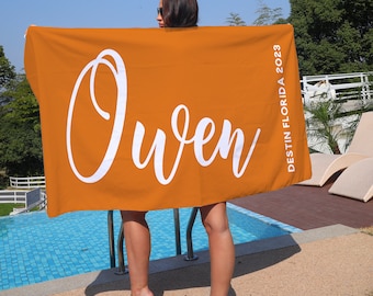 Puede incluir: Una toalla de playa de color naranja brillante con el nombre "Owen" escrito en letras blancas en cursiva. La toalla también tiene el texto "Destin Florida 2023" impreso en el lado derecho.