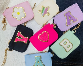 May include: A set of eight small zippered pouches with various colorful fabrics and gold chains. Each pouch features a different embroidered design, including a flower, a star, a heart, and letters A, B, and Y.