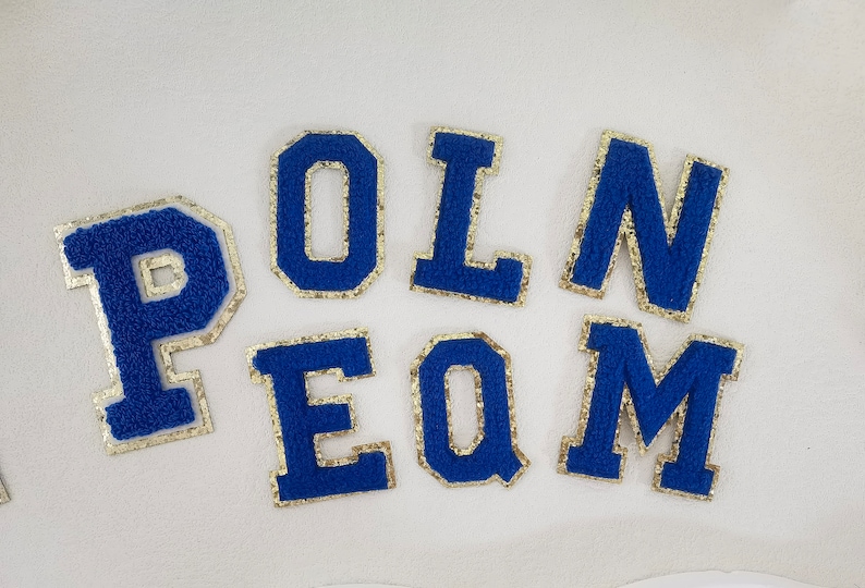 May include: Blue felt letters with gold trim spelling out the word "POLN EQM".