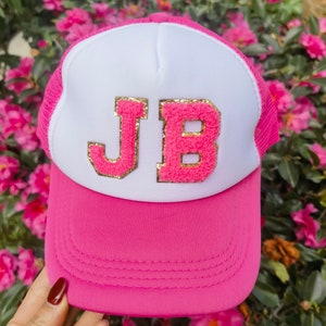 May include: A pink and white trucker hat with the letters "JB" in gold glitter on the front.