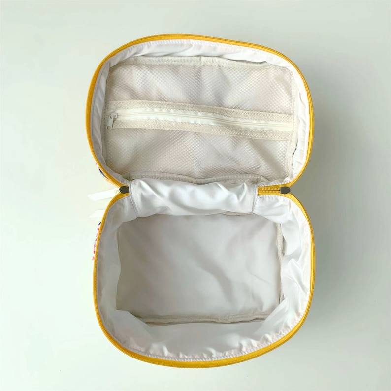 May include: Open yellow cosmetic bag with a white interior and a zippered mesh pocket. The bag has a yellow zipper and a white lining. The bag is open, revealing the inside.