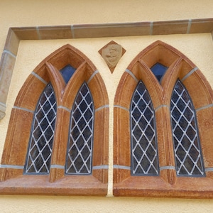 May include: Two arched windows with diamond-shaped glass panes, framed in brown stone, set into a yellow wall.