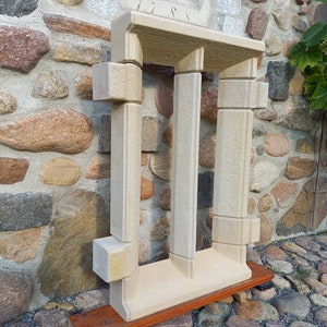 May include: A white stone archway with three pillars, resembling a miniature version of a classical building. The archway is displayed on a wooden base.