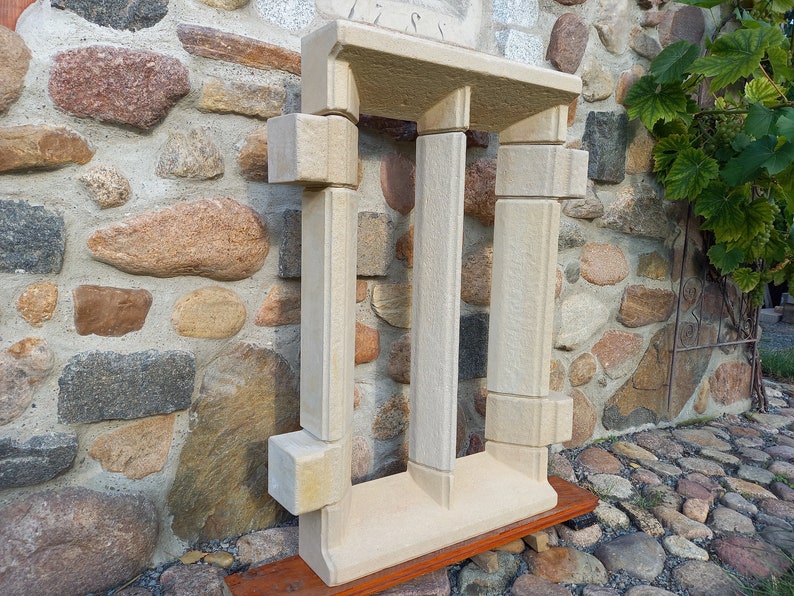 May include: A white stone archway with three pillars, resembling a miniature version of a classical building. The archway is displayed on a wooden base.