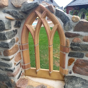 May include: A stone wall with a decorative archway made of brown and red brick. The archway has a pointed top and three vertical panels. The archway is set into the wall and looks out onto a grassy area.