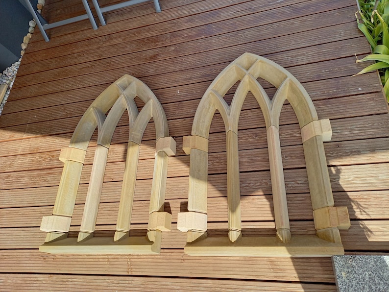May include: Two unfinished wooden arched window frames, each with three arched openings, are laid out on a wooden deck. The frames are made of multiple pieces of wood, and the arches are formed by overlapping pieces of wood.