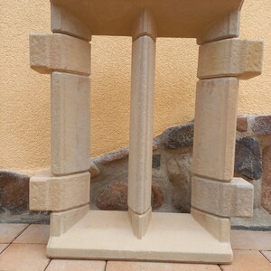 May include: A beige concrete window frame with a decorative design. The frame is made of multiple pieces of concrete that are stacked on top of each other.