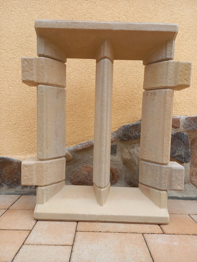 May include: A beige concrete window frame with a decorative design. The frame is made of multiple pieces of concrete that are stacked on top of each other.