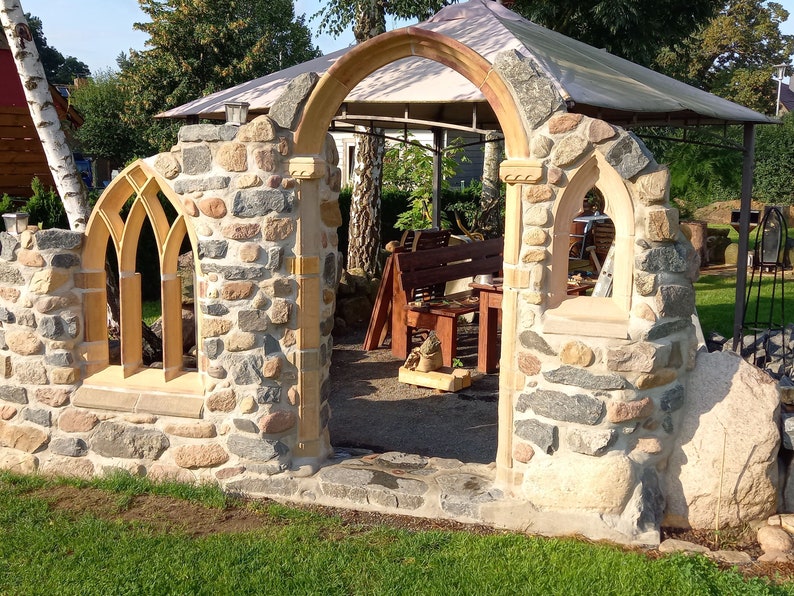 May include: A stone archway with a wooden frame and a stone wall on either side. The archway is made of rough-hewn stones and has a rustic look. The wall is made of smaller stones and has a more polished look.