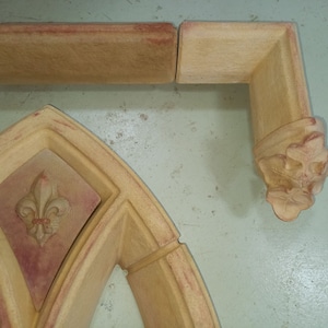 May include: A set of decorative architectural moldings made of plaster or stone. The moldings feature a fleur-de-lis design and are painted in shades of beige and brown.