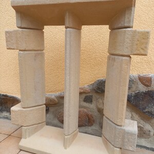 May include: A beige stone window frame with a double-pane design. The frame is made of multiple pieces of stone that are stacked on top of each other.