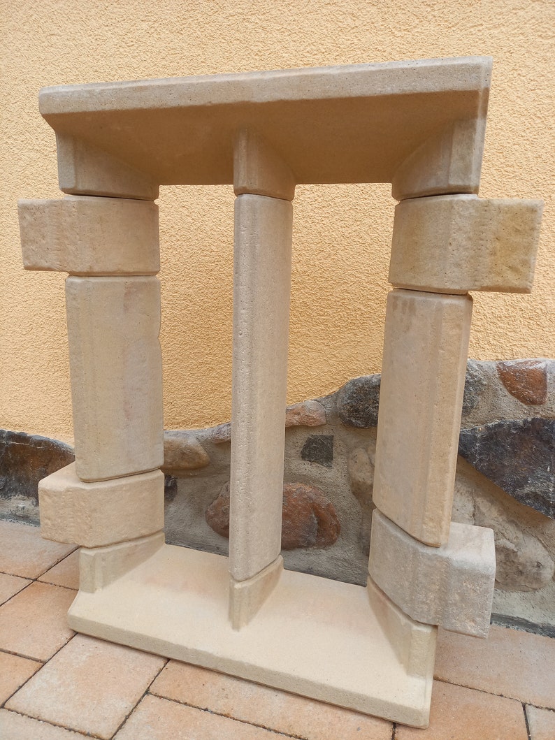 May include: A beige stone window frame with a double-pane design. The frame is made of multiple pieces of stone that are stacked on top of each other.