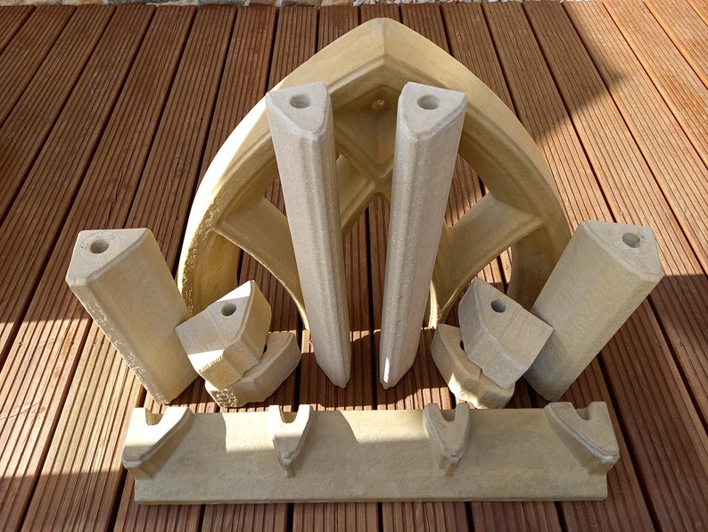 May include: A set of beige stone pieces that can be assembled to create a decorative archway. The pieces are designed to fit together to create a pointed arch shape.