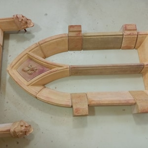 May include: A set of terracotta-colored ceramic pieces that can be assembled to create a decorative arched window frame. The frame features a fleur-de-lis design.