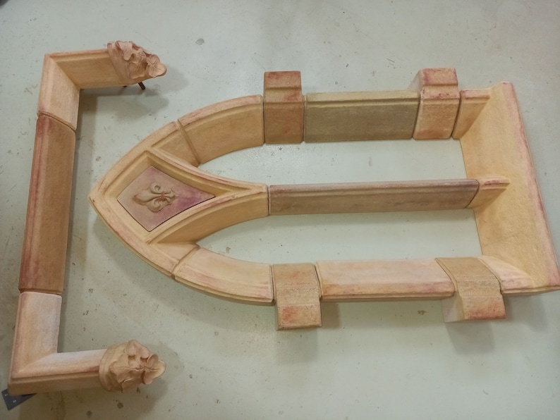 May include: A set of terracotta-colored ceramic pieces that can be assembled to create a decorative arched window frame. The frame features a fleur-de-lis design.