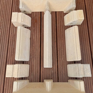 May include: A set of eight beige stone fireplace surround pieces. The pieces are shaped to create a rectangular opening for a fireplace.